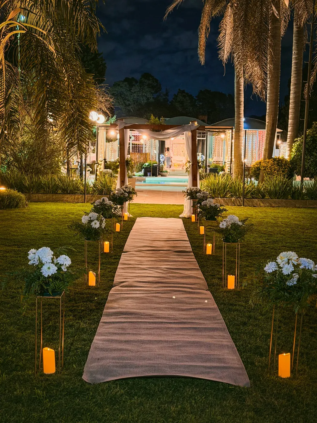 Pasillo de ceremonia con velas, flores blancas y arco al fondo, de noche