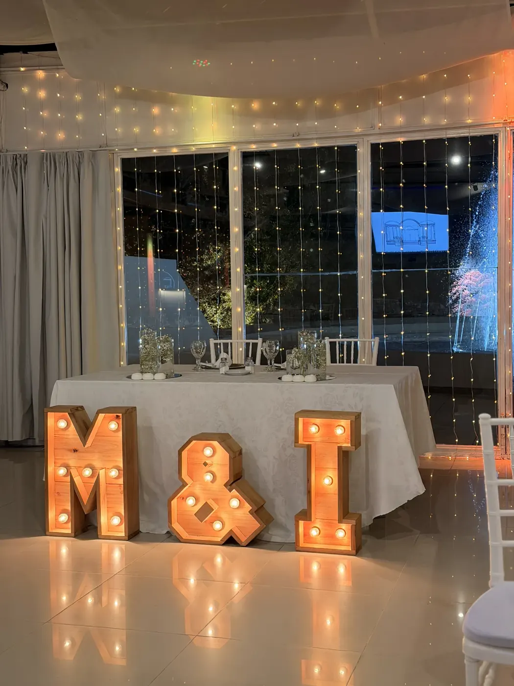 Letras luminosas M&I frente a un ventanal, en una fiesta