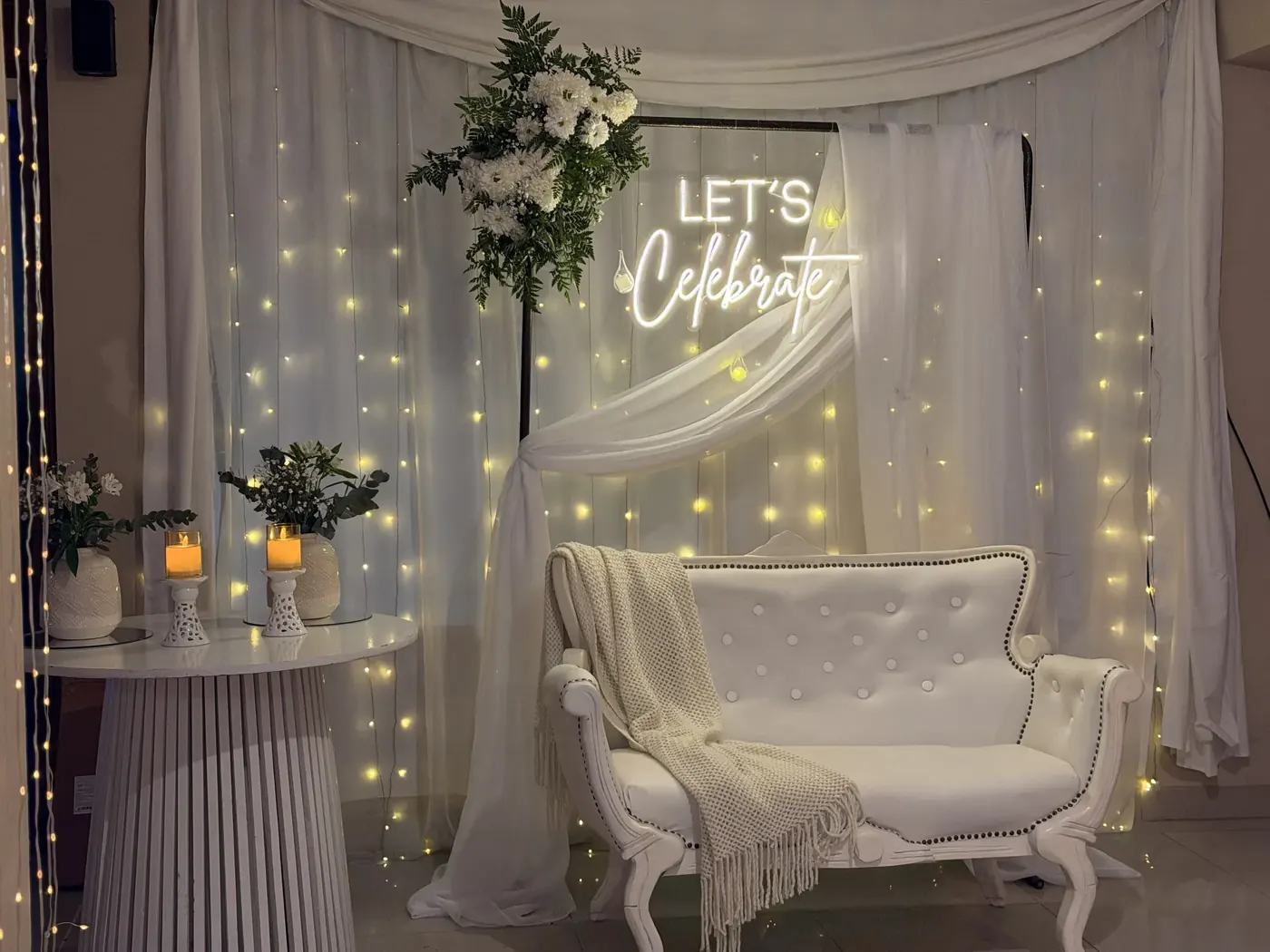 Sillón blanco con manta, mesa y cortina de luces cálidas