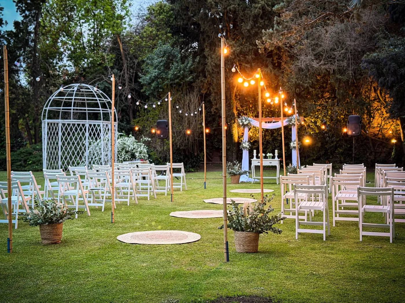 Ceremonia en el jardín al atardecer con sillas blancas y guirnaldas de luces
