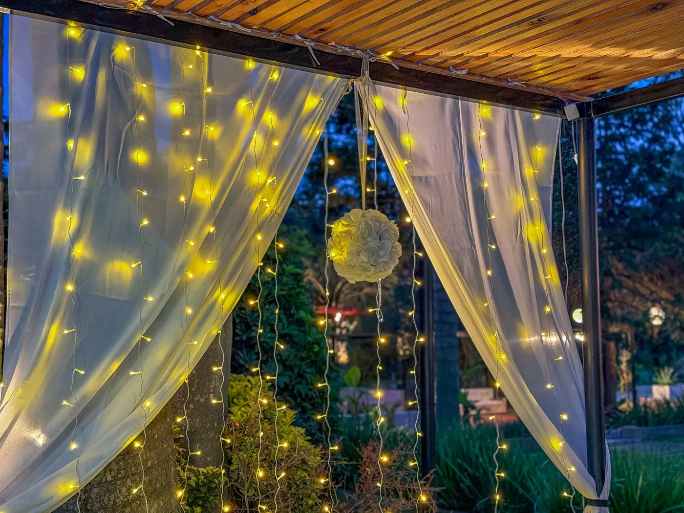 Cortinas de gasa con cortina de luces cálidas bajo una pérgola de madera