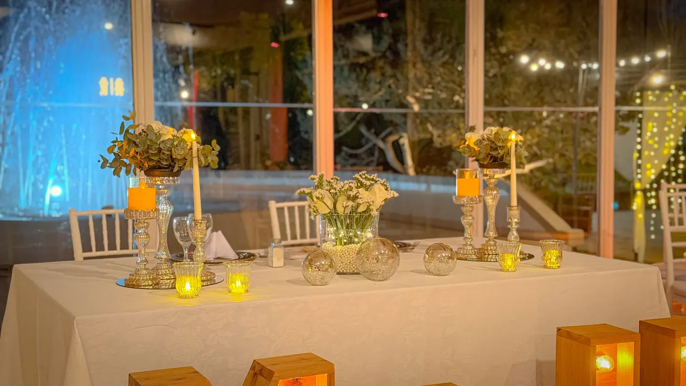 Mesa de recepción con cortinas, velas y luces cálidas junto a la pileta