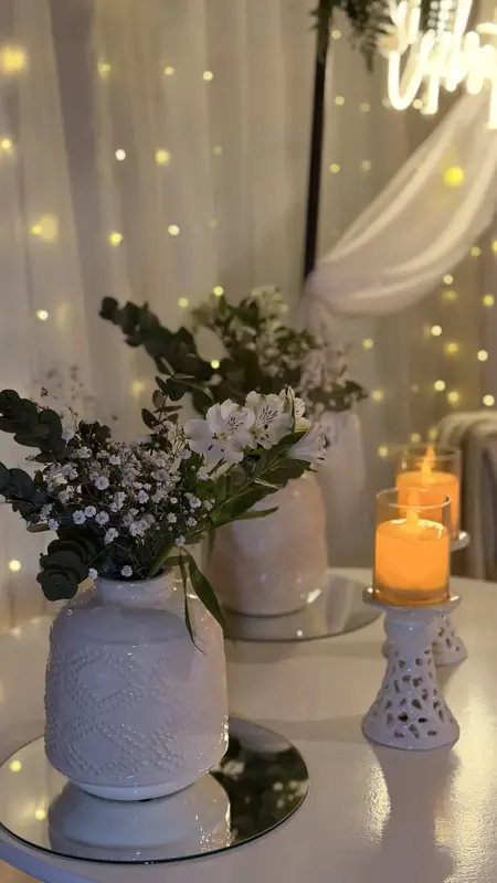 Florero blanco con flores silvestres y velas sobre un espejo
