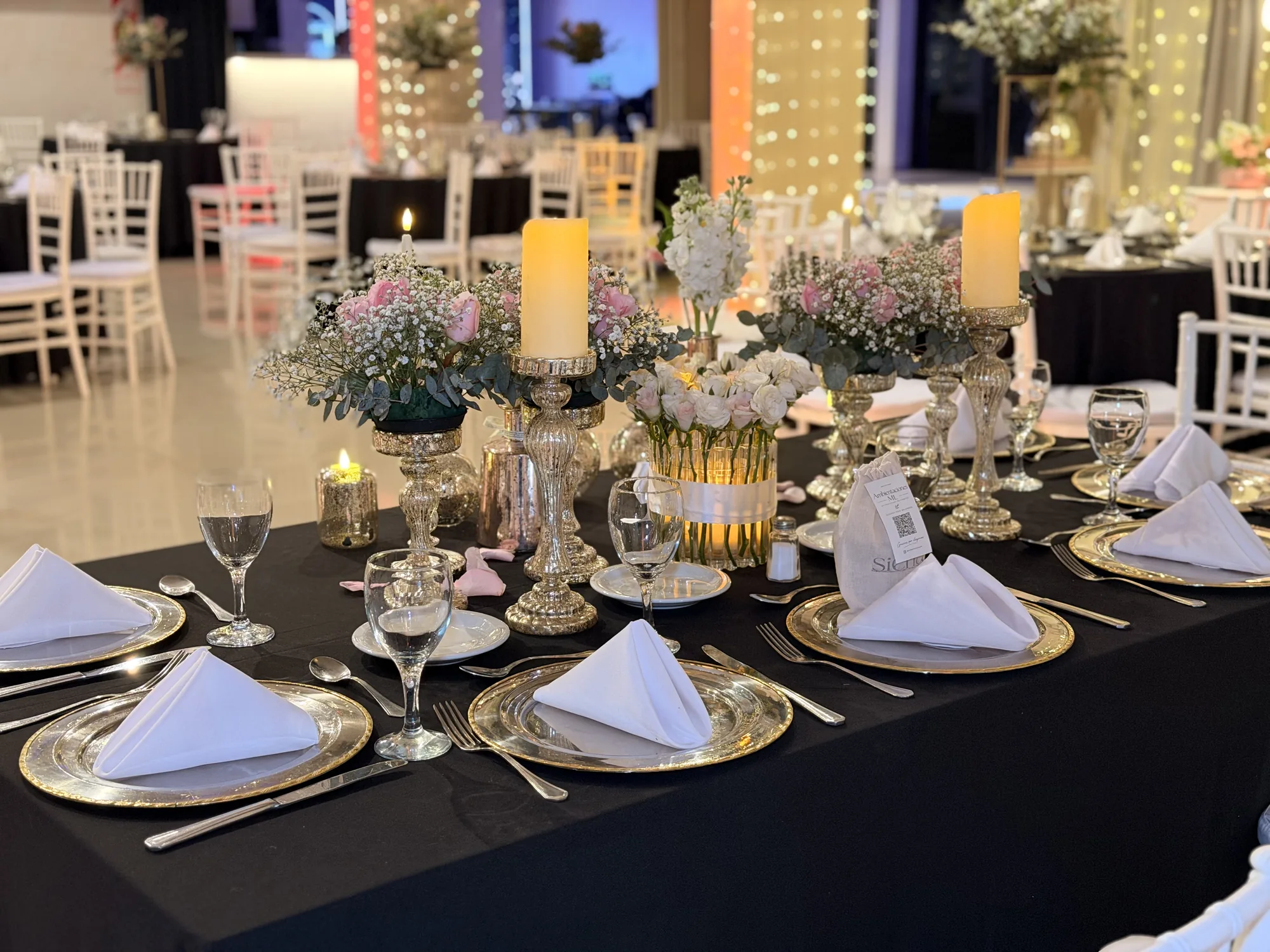 Mesa de fiesta con platos dorados, velas y centros de flores